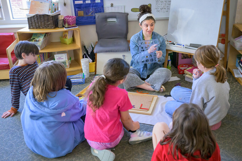 Teacher Olivia Baldacci sits on the floor with students at First State Montessori Academy.