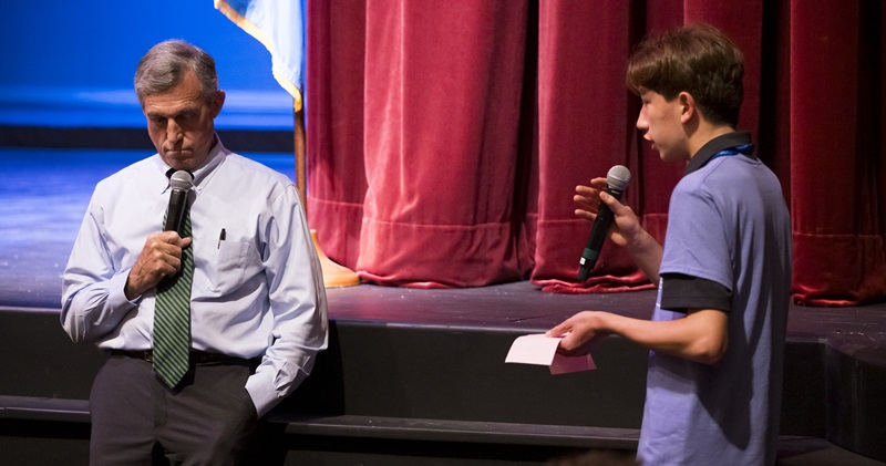 A ttenage boy holds microphone as he speaks to the governor, who listens intently