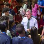 A large group of young students gathers around the governor.