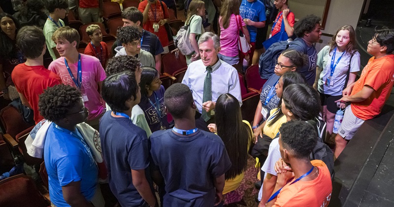 A large group of young students gathers around the governor.