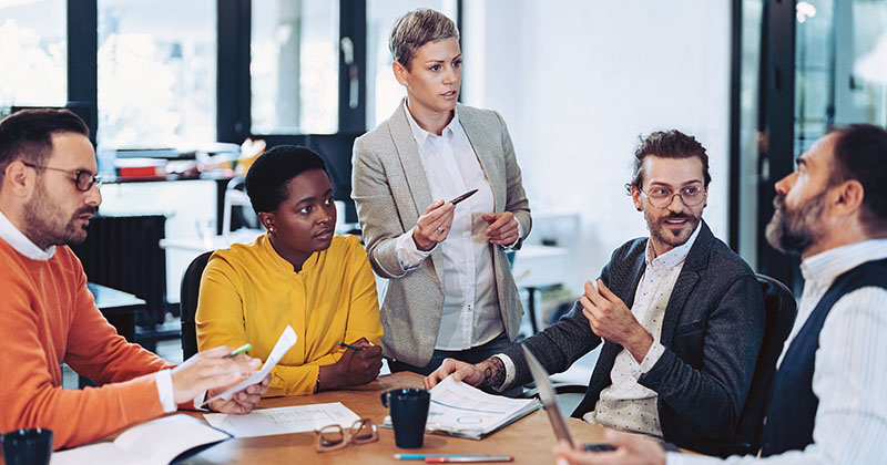 Multiracial group of business people sitting around a table and talking in an open office space.