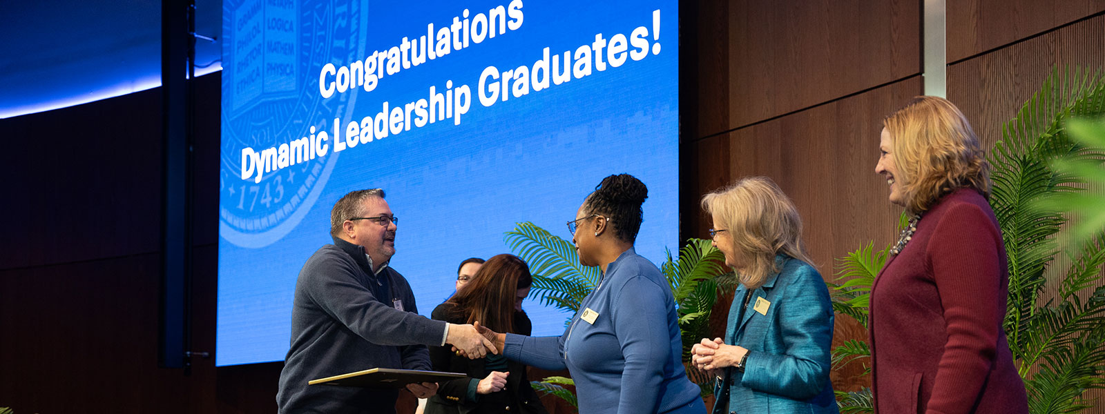 Student graduate crosses stage and receives congratulatory handshakes from program instructors