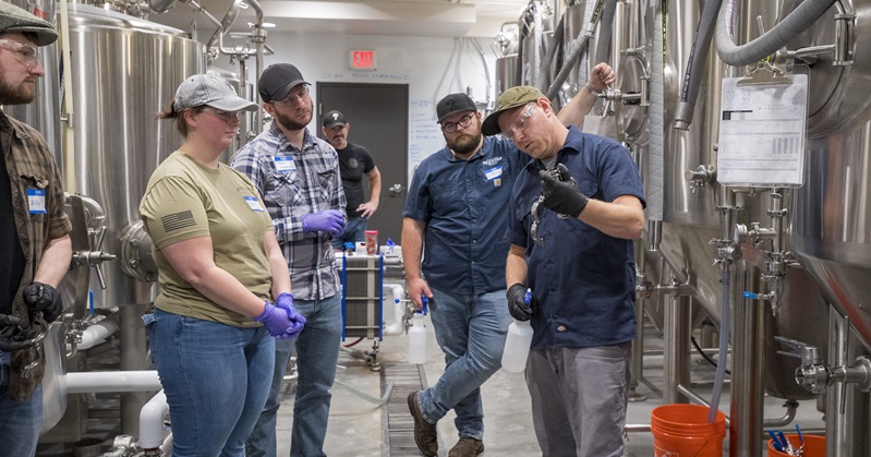 Surrounded by big silver vats, the teacher at Brewing Science course explains the workings of a brewery to his students.