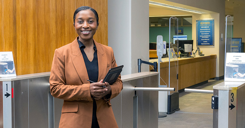 Joy Dufitumukiza standing in front of the turnstiles at the entrance to the Morris Library.