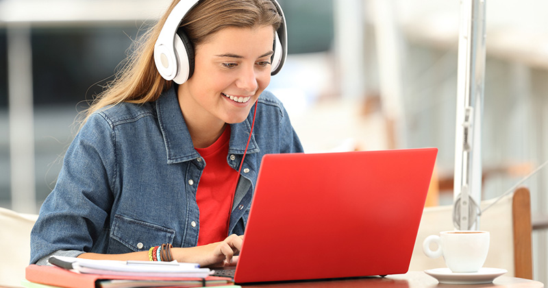 Young girl sitting at a kitchen table working on her laptop with headphones on.